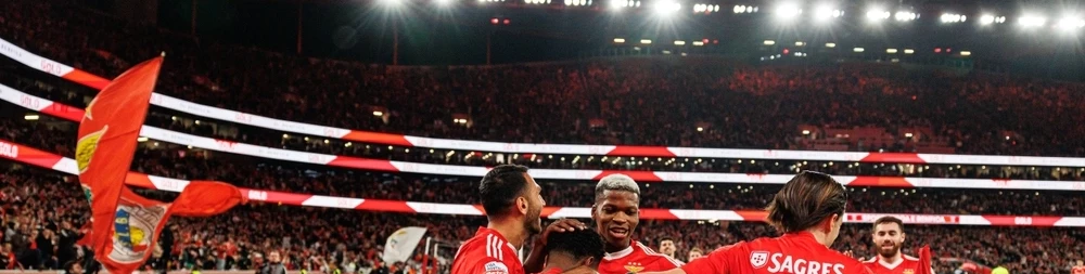 Spieler von Benfica Lissabon bejubeln gemeinsam ein Tor an der Eckfahne vor einer riesigen, rot erleuchteten Stadionkulisse. Erleben Sie den portugiesischen Spitzenfußball live bei einer organisierten Fanreise.