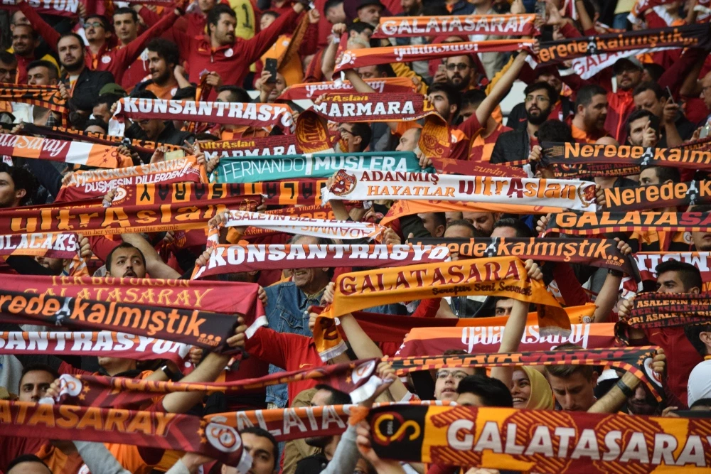 Zahlreiche Fußballfans auf einer vollbesetzten Stadiontribüne halten stolz rot-gelbe Fan-Schals in die Höhe. Die leidenschaftliche Stimmung macht eine Fußballreise in die Türkei zu einem unvergesslichen Erlebnis.