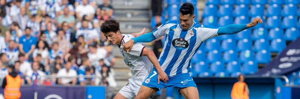 Wedstrijdactie tijdens een Galicisch duel Twee voetballers in een fel duel om de bal, met op de voorgrond een speler in het blauw-wit gestreepte shirt van Deportivo de La Coruña.